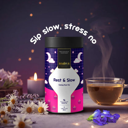 Rest & Slow herbal tea by Innofus for sleep and stress relief, calming blend with lavender, chamomile, blue pea; nighttime mood, steaming tea cup, candle, flowers and “Sip slow, stress no” tag.