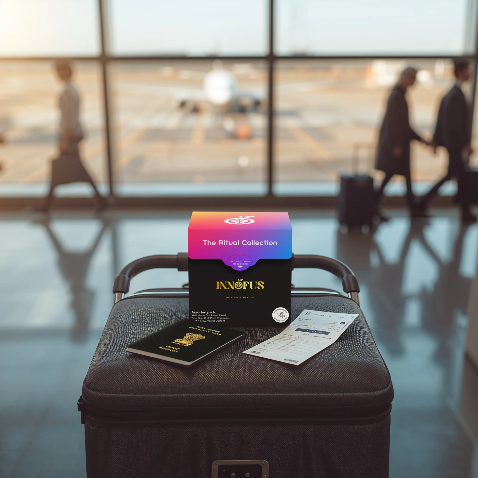 The Ritual Collection by Innofus, colorful tea bag assortment box displayed on airport luggage with passport and boarding pass, blurred travelers and airplane in background, travel wellness tea concept.
